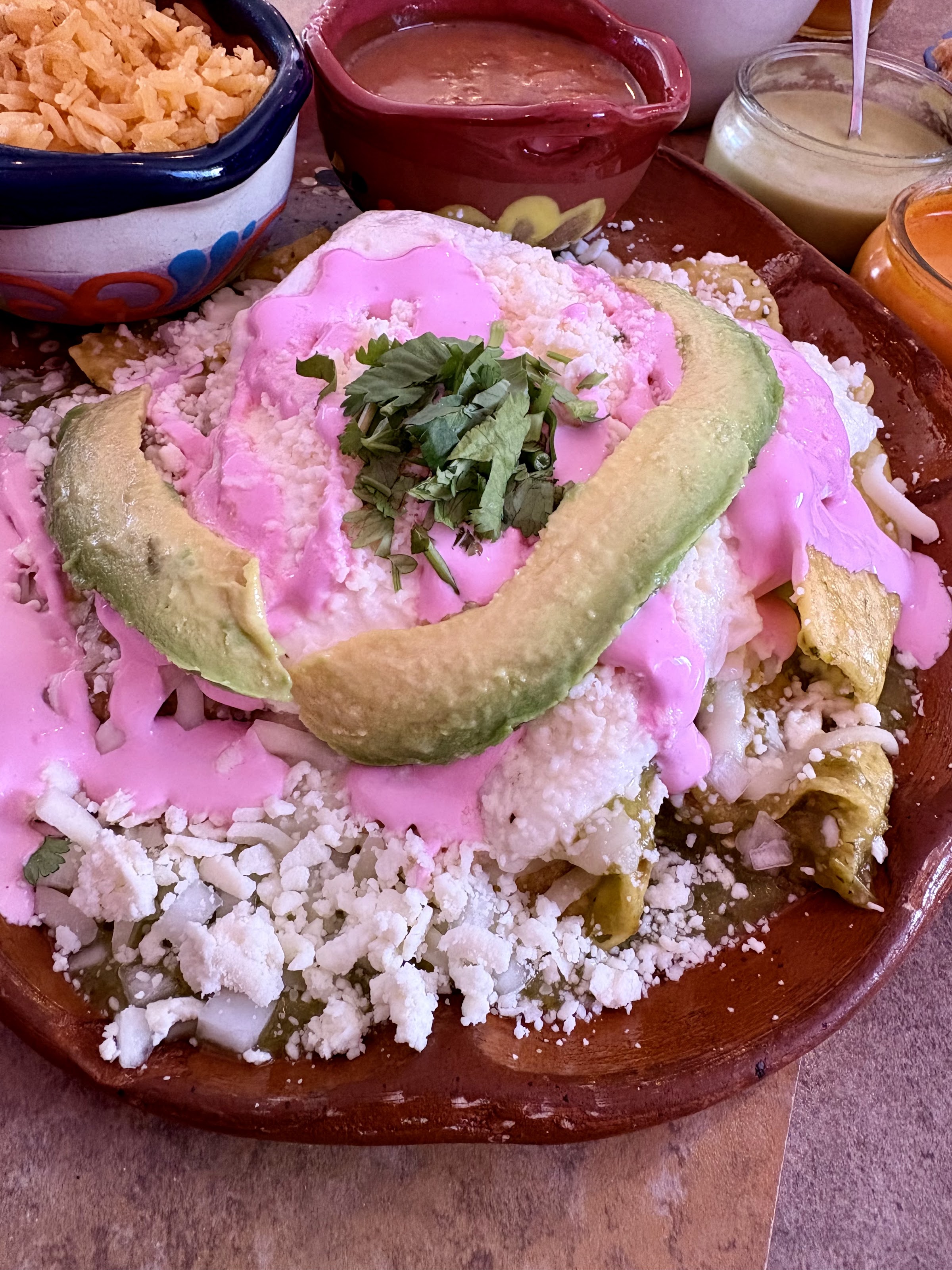 Chilaquiles verdes drenched in the house pink crema sauce with a fan of avocado on a clay plate